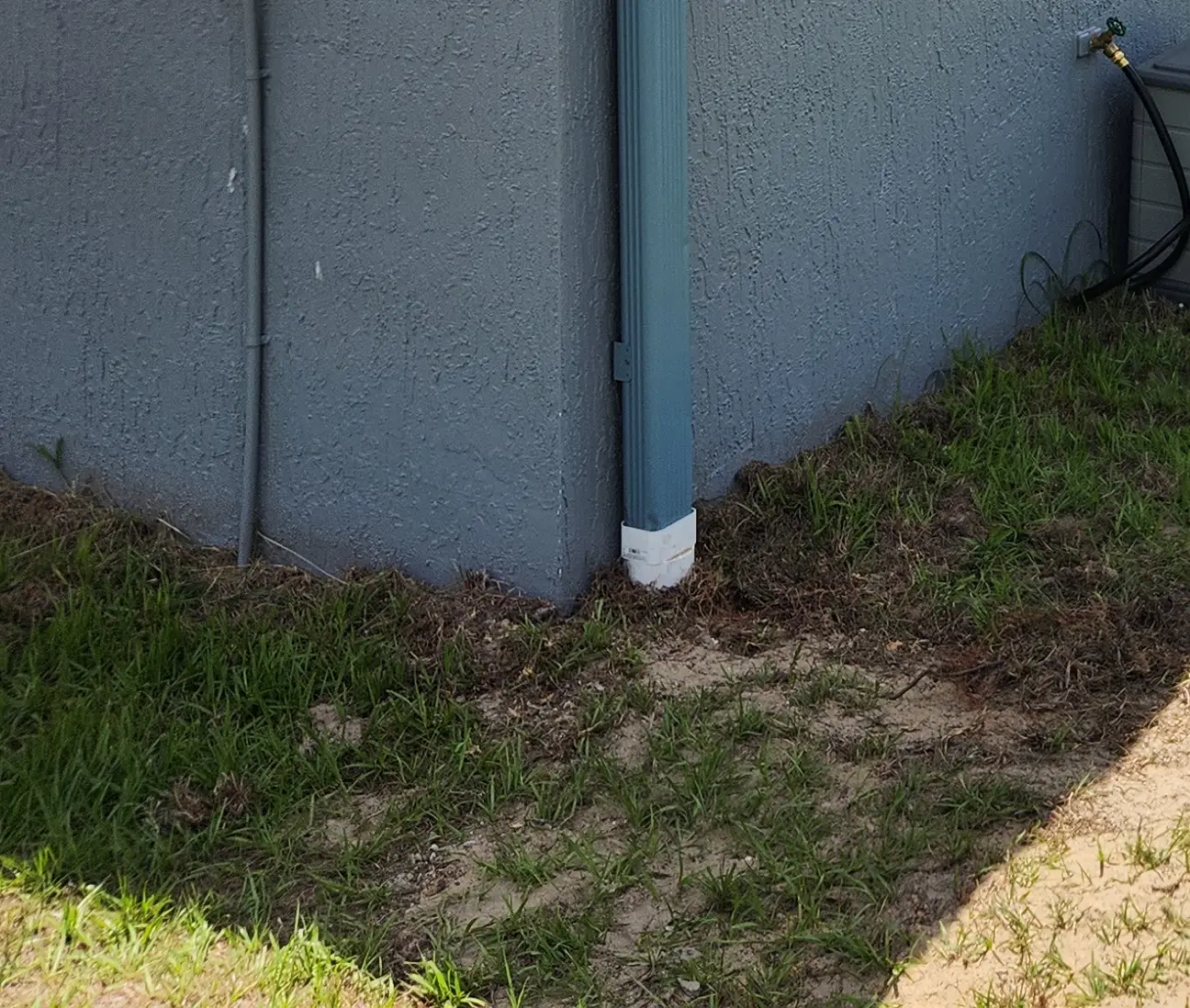 White downspout discharging at the base of a stucco wall, where underground drainage is needed