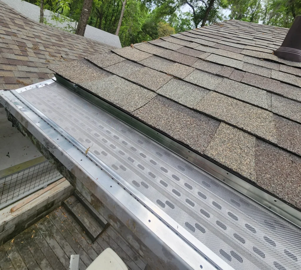 Perforated micro-mesh leaf guard installed along a seamless gutter under a shingle roof