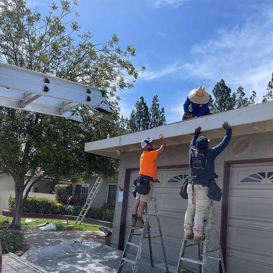 Crew on ladders installing fascia along a garage roofline